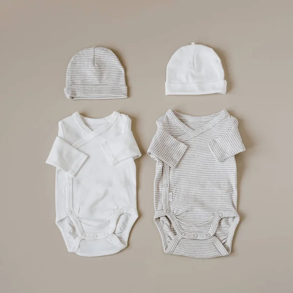新生児のための居心地の良い巨大な服やアクセサリー 基本的なボディスーツ パステルベージュの背景の帽子 審美的なミニマリストの赤ちゃんファッションコラージュ — ストック写真