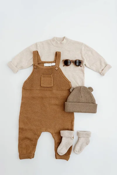 Cute gender neutral baby clothes. Knitted jumpsuit, sweater, kids sunglasses, socks, warm hat. Stylish elegant neutral pastel colours newborn baby clothes, accessories. Flat lay, top view