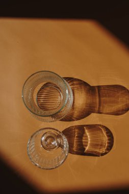 Turuncu arka planda cam ve cam vazo ve güneş ışığı gölgeleri. Düz yatış, üst görünüm