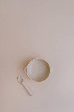 Silicone bowl and spoon for little baby kid to eat food on light pastel pink background. Flat lay, top view