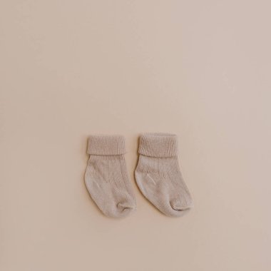 Pair of cozy hygge pastel colourful newborn baby socks on neutral beige background. Aesthetic minimalist baby fashion collage. Happy maternity concept