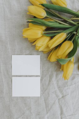 Blank paper sheet cards with mockup copy space and yellow tulip flowers bouquet on neutral crumpled linen cloth background. Aesthetic minimalist business brand template. Flat lay, top view