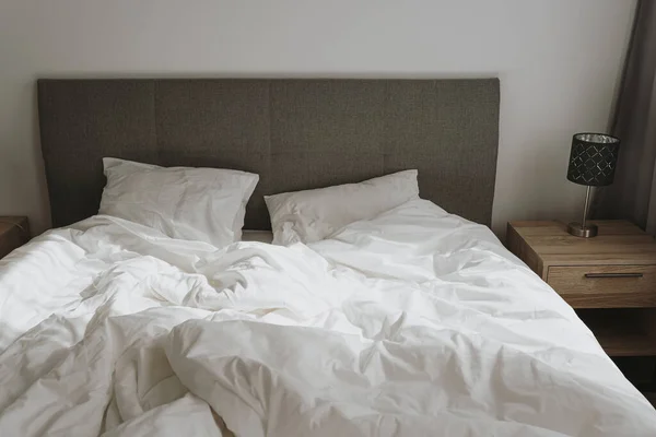 Aesthetic minimal home, bedroom interior design. Bed with crumpled white bed linens, pillows, sunlight shadows