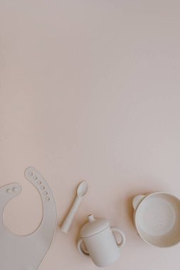 Silikon kase, kaşık, önlük, küçük bebek için yiyecek ve içecek. Açık renkli pembe arka plan. Düz yatış, üst görünüm