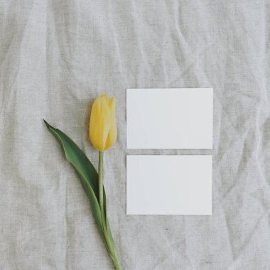 Boş kağıt davetiye kartları. Tarafsız, buruşuk kumaş arkaplanda sarı lale çiçeği. Düz konum, üst görünüm minimal çiçek bileşimi