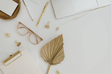 Flatlay of gold female accessories and office stuff. Comfortable home office workspace. Work at home. Laptop computer, clipboard, fan leaf stem, glasses, clips, pen on table. Flat lay, top view clipart