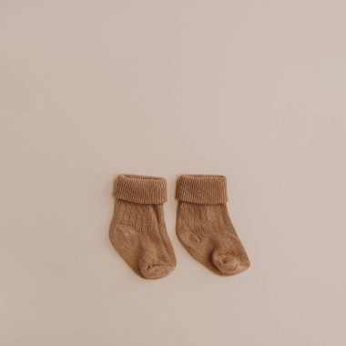 Pair of cozy hygge pastel colourful newborn baby socks on neutral beige background. Aesthetic minimalist baby fashion collage. Happy maternity concept