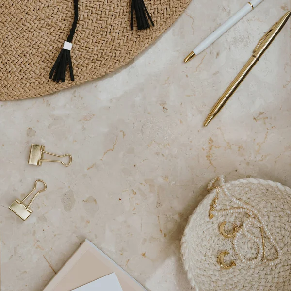 Straw hat, gold accessories on marble table with blank mockup copy space. Stylish fashion flat lay, top view minimalist home office desk workspace template