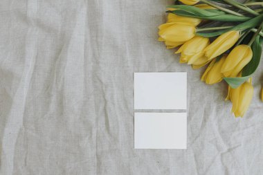 Blank paper sheet cards with mockup copy space and yellow tulip flowers bouquet on neutral crumpled linen cloth background. Aesthetic minimalist business brand template. Flat lay, top view