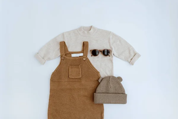 Cute gender neutral baby clothes. Knitted jumpsuit, sweater, kids sunglasses, socks, warm hat. Stylish elegant neutral pastel colours newborn baby clothes, accessories. Flat lay, top view