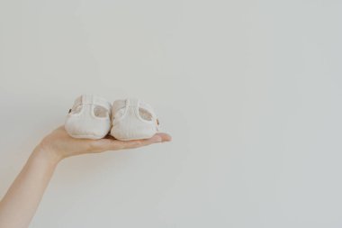 Beyaz arka planda küçük sevimli bebek sandaletleri tutan birinin eli. Minimalist bebek kıyafeti.