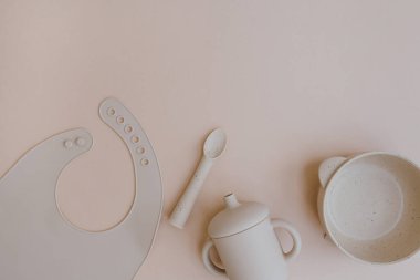 Sevimli bebek sofra takımı ve silikon önlük. Tabak, önlük, kupa, tarafsız arka planda kaşık. Bebek ilk yemek aksesuarlarını servis ediyor. Düz yatış, üst görünüm beslenme ve beslenme konsepti