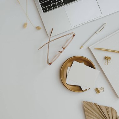 Düz dizüstü bilgisayar, boş kart kağıdı, gözlük, yelpaze yaprağı, beyaz arka planda altın aksesuarlar. Üst düzey minimalist estetik çalışma alanı, iş konsepti. Boşluğu kopyala
