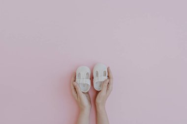 Person's hands hold cute little baby sandals shoes on pastel pink background. Minimalist baby fashion apparel