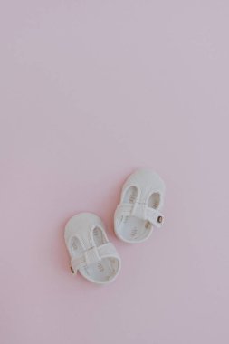 Tarafsız pastel pembe arka planda bir çift çocuk ayakkabısı. Düz yatıyordu, İskandinav tarzı bebek kıyafetleri.