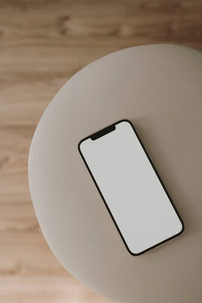 Mobile phone on beige stool. Flat lay, top view. Aesthetic copy space mockup template.