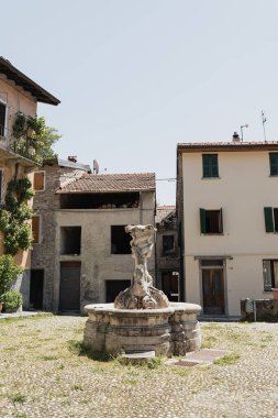 Eski İtalyan köyü mimarisi. Geleneksel Avrupa binaları. Çeşme, ahşap pencereler, kepenkler, nötr renk duvarlar