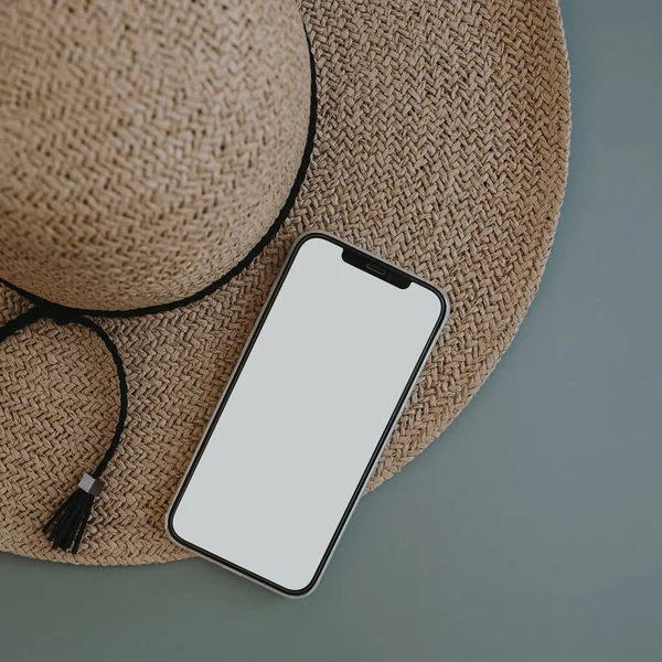 Flatlay of aesthetic women\'s fashion accessories. Mobile phone with blank copy space screen. Stylish female straw hat on pastel blue copy space background. Top view, flat lay online shopping