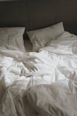 Yatak odası konsepti. Beyaz buruşuk çarşafları, yastıkları olan rahat bir yatak. Güneş ışığı yansımaları. Sabah yatakta