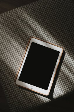 Güneş ışığı gölgesi ile klasik kumaş desenli arka plan üzerinde kopyalama alanı olan boş ekran tableti. Düz yerde, üst tarafta. Boşluk düzenleme şablonunu kopyala.