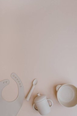 Silikon kase, kaşık, önlük, küçük bebek için yiyecek ve içecek. Açık renkli pembe arka plan. Düz yatış, üst görünüm