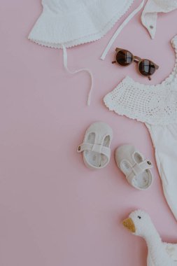 Beyaz elbise, panama şapkası, güneş gözlüğü, sandalet, oyuncak ördek. Bebek kıyafetleri ve aksesuarlar pembe arka planda. Moda İskandinav yeni doğan kıyafetleri. Düz yatış, üst görünüm