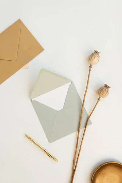 Flatlay invitation cards, craft envelopes, poppy stems, pen on white background. Flat lay, top view