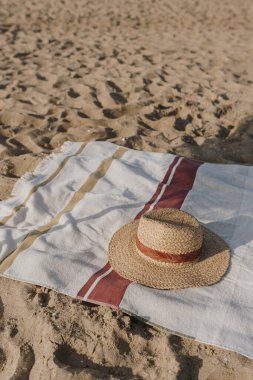 Plaj kumsalında kadın hasır şapka ve plaj havlusu. Asgari estetik yaşam tarzı moda blogu, dergi, sosyal medya. Güneş banyosu, dinlenme, yaz tatillerinde serinleme.