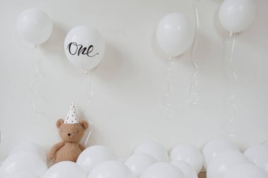Balonlu oyuncak ayı beyaz arka planda balonların yanında oturuyor.