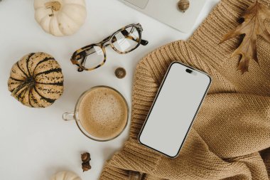 Boş ekran cep telefonu, dizüstü bilgisayar, kahve fincanı, bardak, bal kabağı, bej kumaş beyaz masa. Freelancer veya moda blogcusu ev çalışma alanı