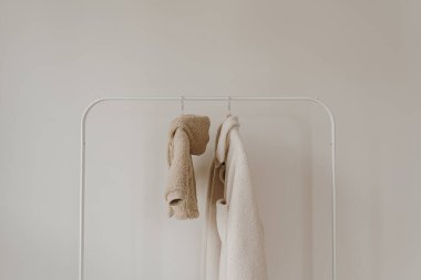 Sonbahar kıyafetleri beyaz duvardan sarkıyor. Sıcak bebek ve yetişkin ceketleri. Kıyafetleri tarafsız renklerde olan estetik bir gardırop.