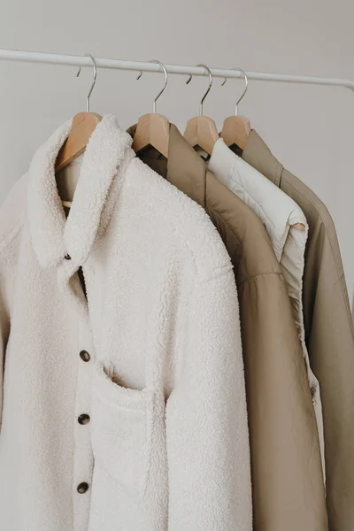 Warm autumn seasonal women\'s clothes on hanger over white wall. Neutral beige jackets and coat. Minimalist fashion clothes wardrobe