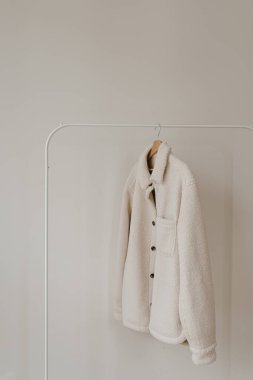 Beyaz duvarda asılı duran beyaz, sıcak, yünlü sonbahar sezonu ceketi. Minimalist moda kıyafet dolabı.