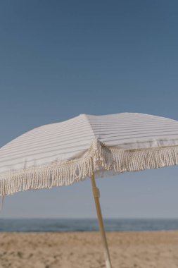 Mavi gökyüzünün, kumsalın ve denizin önündeki kumsal şemsiyesi