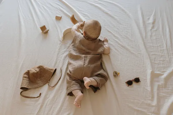 ベージュのベッドリネンの上に横たわる茶色のリネンのボディスーツでかわいい新生児 審美的な赤ちゃんのファッション組成物 フラットレイアウト トップビュー — ストック写真