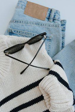 Şık, sıradan kadın kıyafetleri ve aksesuarları. Estetik minimal moda kompozisyonu. Çizgili kazak, kot pantolon, güneş gözlüğü. Düz yatış, üst görünüm