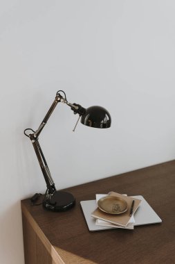 Masa lambası, defterler, beyaz duvarın yanındaki tahta masada dizüstü bilgisayar. Minimalist ev ofis çalışma alanı. Evde çalışmak, eğitim kavramı