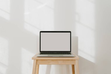 Boş ekranlı dizüstü bilgisayar ve duvarında güneş ışığı gölgeleri. Asgari biçimdeki web sitesi, çevrimiçi dükkan, mağaza, taklit alanı olan sosyal medya şablonu