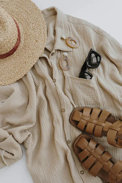 Flatlay of elegant stylish women\'s beach clothes and accessories. Aesthetic luxury summer fashion composition. Muslin t-shirt, straw hat, leather sandals, sunglasses, earrings. Flat lay, top view