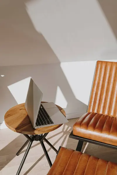 Luxury minimal interior design concept. Bright modern Scandinavian home office workspace with laptop computer, leather lounge armchair and sunlight shadows on the wall