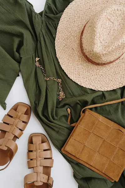 Flatlay of elegant stylish women\'s clothes and accessories. Aesthetic luxury fashion composition. Green evening dress, straw hat, leather sandals, purse, suede bag, necklace. Flat lay, top view