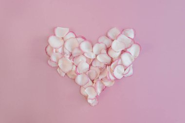 Sevgililer Günü kompozisyonu. Soluk renkli pembe arka planda gül yapraklarından yapılmış kalp. Düzlük, üst görünüm aşk konsepti
