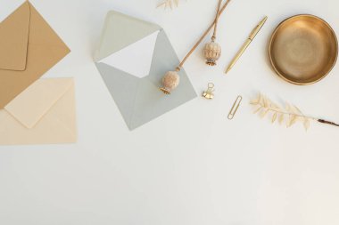 Tatil davetiyesi. Boş kağıt tebrik kartı, el işi zarfı, kurutulmuş haşhaş sapları, beyaz arka planda kırtasiye malzemesi. Düz yatış, üst görünüm