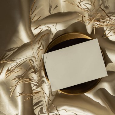 Kağıt kağıtta boş kopya alanı ve parlak altın sarısı ipek arka planda kurutulmuş çimenler. Estetik güneş ışığı gölge silueti. Lüks bohem asgari davet veya kartvizit şablonu