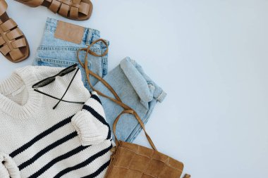 Şık, sıradan kadın kıyafetleri ve aksesuarları. Estetik moda kompozisyonu. Çizgili kazak, süet çanta, kot pantolon, deri sandalet, güneş gözlüğü. Düz yatış, üst görünüm