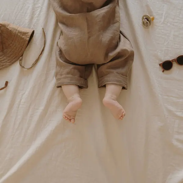 中立ベージュベッドのリネンにアクセサリーが付いているスタイリッシュな基本ボディスーツの新生児 ファッション スカンジナビアの新生児の服 おしゃぶり サングラス フラットレイ トップビュー — ストック写真