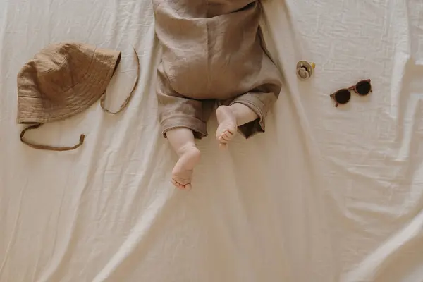 ベージュベッドのリネンでベッドの上に横たわっている茶色のボディスーツのかわいい新生児 かわいいミニマルベビーファッションコンセプト トップビュー — ストック写真