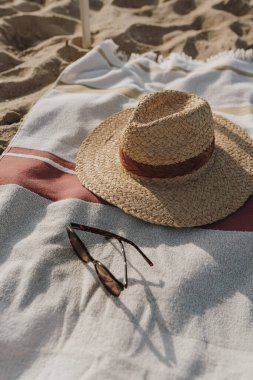 Kadın güneş gözlüğü, hasır şapka ve kumsalda havlu. Asgari estetik yaşam tarzı moda blogu, dergi, sosyal medya. Güneş banyosu, dinlenme, yaz tatillerinde serinleme.