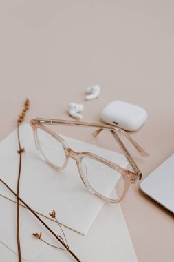 Estetik stil kadınlar için ofis çalışma masası. Gözlükler, kulaklıklar, zarflar, bej masadaki kurutulmuş çimenler. Ev kavramında zarif modern çalışma