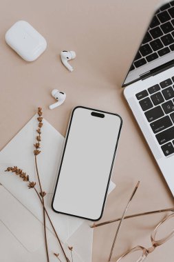 Boş ekranlı cep telefonu, dizüstü bilgisayar, kulaklık, bej masasında kurutulmuş çimen. Biçimlendirilmiş düz, boş kopya alanı ile düzenlensin. Tasarlanmış üst görünüm cep telefonu modeli